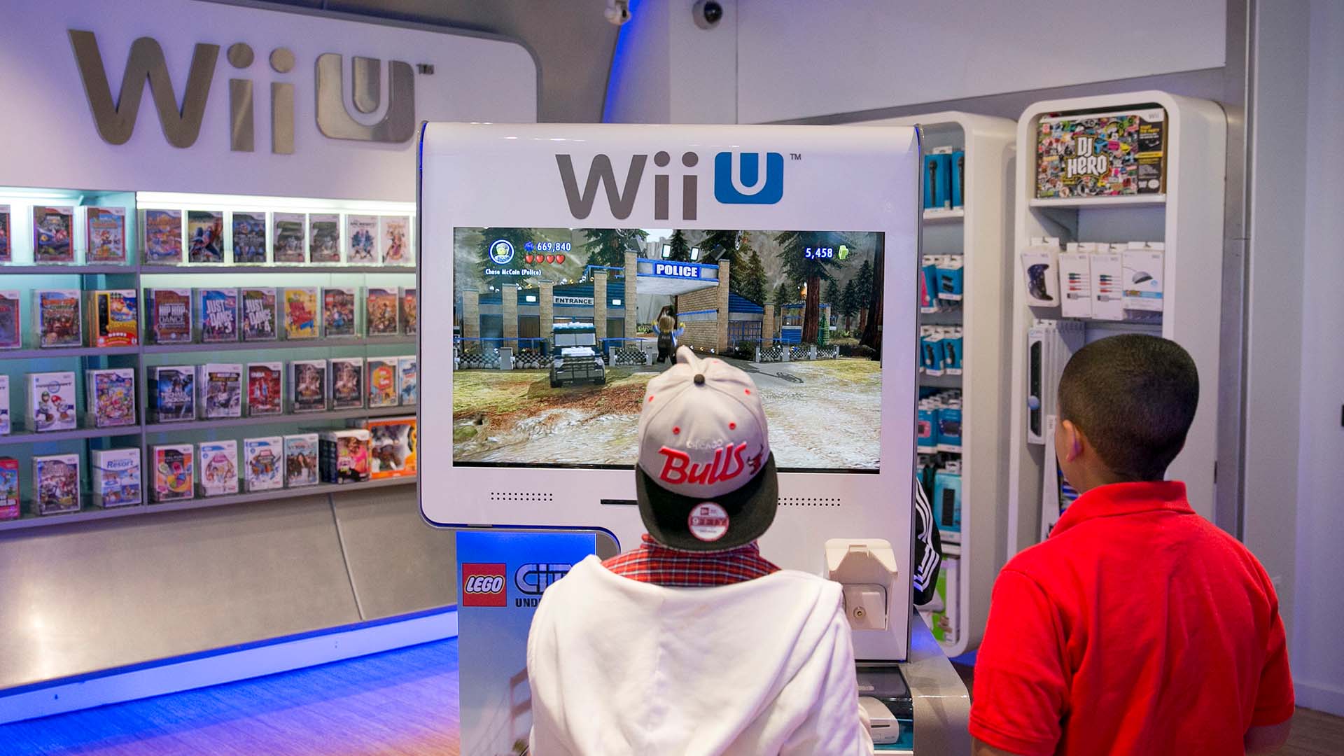 تظهر الصورة طفلين يلعبان بكشك تجريبي لجهاز Wii U في أحد متاجر Nintendo. 